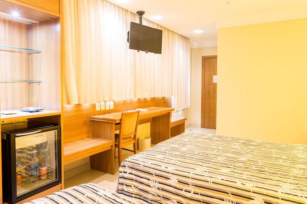 Hotel Atlântico Business Centro Rio de Janeiro Exterior foto The photo shows a hotel room with two beds featuring striped bedding. There is a wooden desk and chair near a window with light-colored curtains. A flat-screen television is mounted on the wall, and there appears to be a small refrigerator or mini-ba