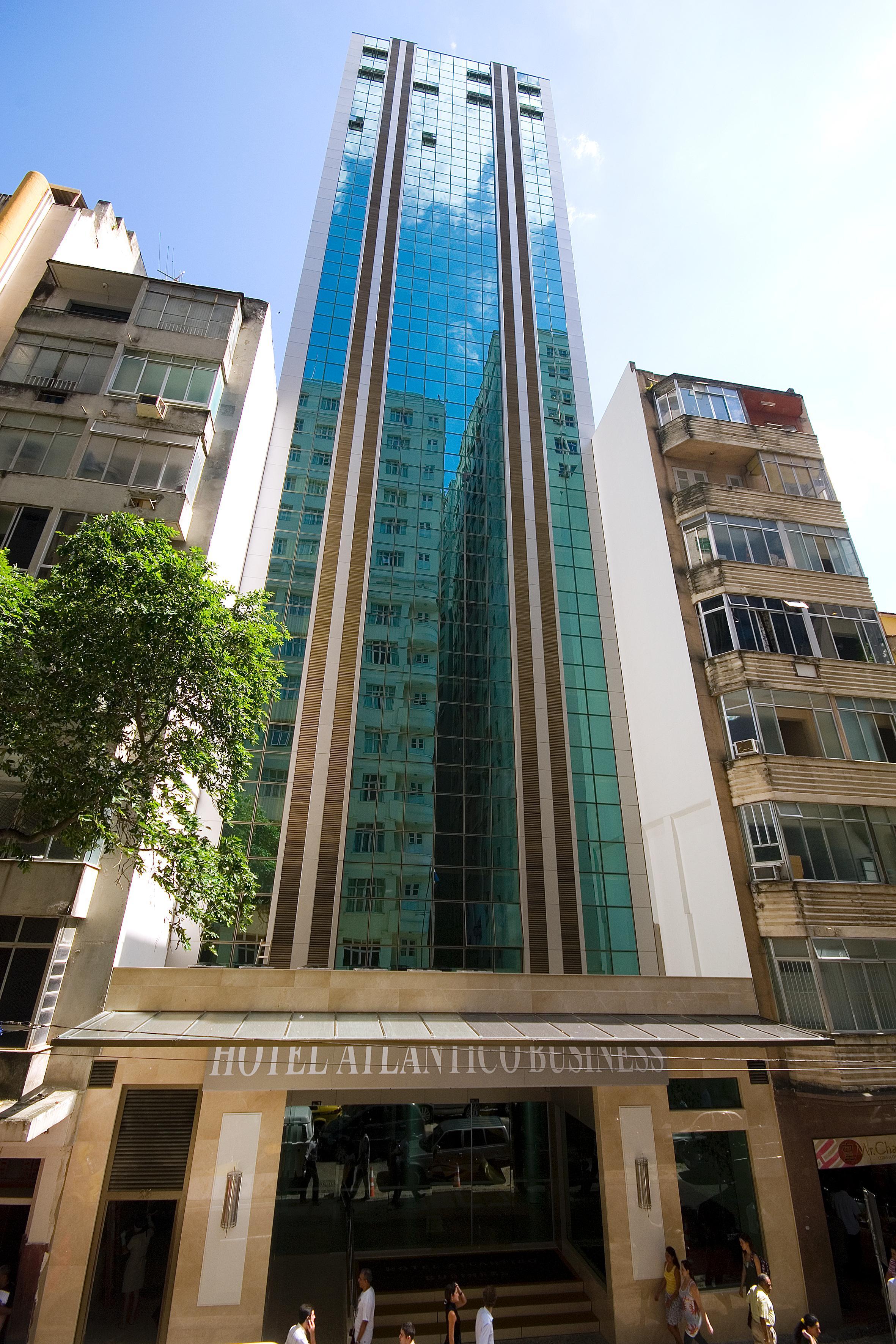 Hotel Atlântico Business Centro Rio de Janeiro Exterior foto The photo shows a modern multi-story building with a sleek glass facade. The building appears to have several floors with large windows, reflecting sunlight, and is flanked by a tree on one side and an older, more traditional residential structure on